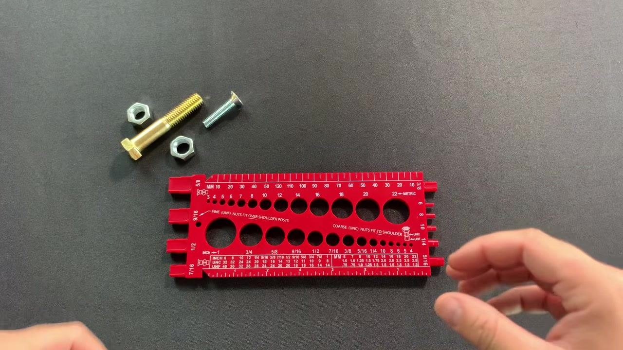 Hands holding the red thread gauge, showing both the metric (top) and inch (bottom) measurement holes and rulers, with bolts and nuts visible in the background.