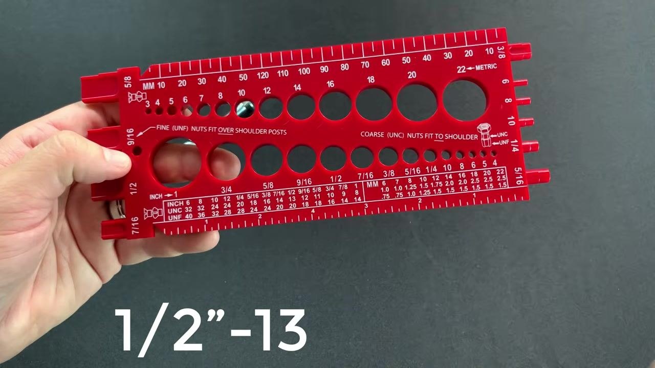 The red gauge held with the ruler edge visible and the gold bolt positioned for length measurement, aligned from the underside of the head.