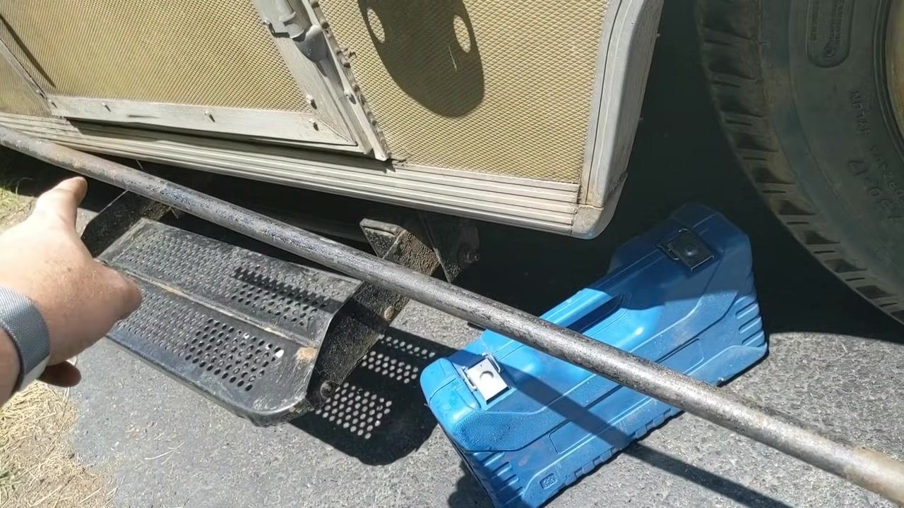 Lug wrench positioned on a lug nut, supported by a jack stand for stability, with the blue tool case visible in the background