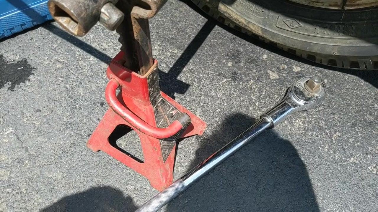 Red jack stand supporting a lug wrench, with a large chrome ratchet and extension pipe lying on the ground nearby