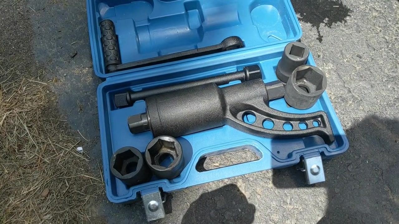 Hand reaching toward a rusty wheel with lug nuts, with the blue torque multiplier kit open, sockets and multiplier visible below