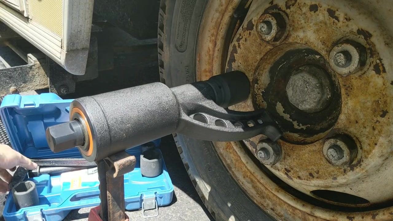 Hands positioning the torque multiplier onto the lug nut, with the blue case and jack stand visible and the handle about to be inserted