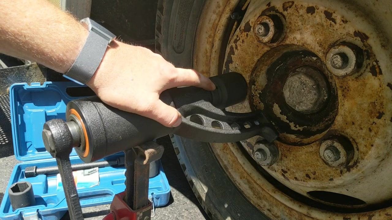 Hand turning the torque multiplier handle as the nut begins to loosen, with the blue case and jack stand visible