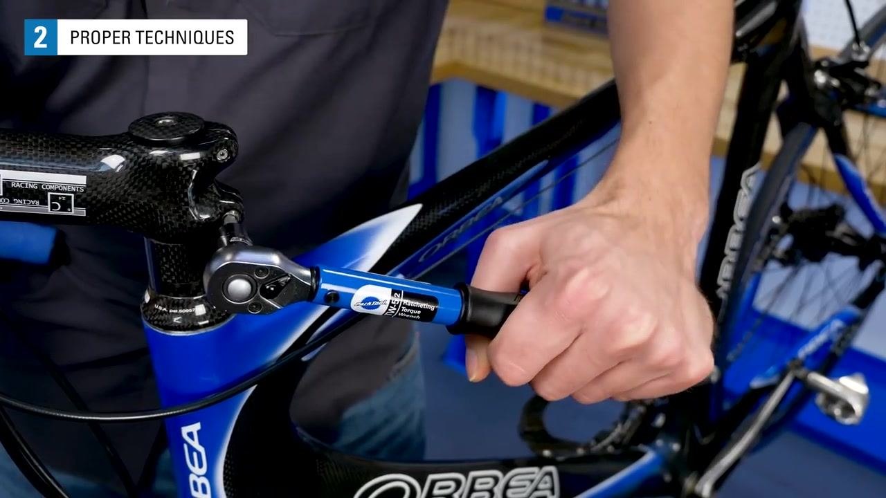 A hand grips the handle of a TW-5.2 torque wrench, applying force to a fastener on a bicycle handlebar.