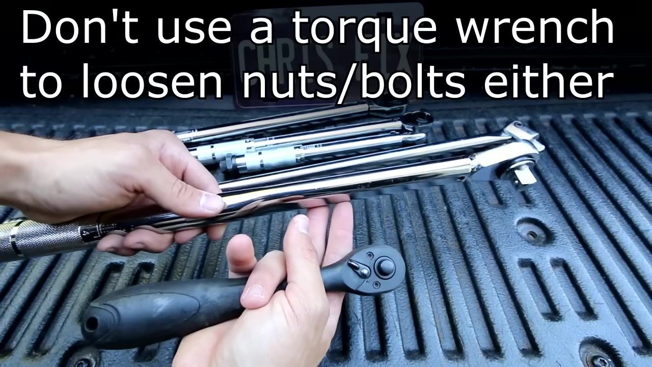 A hand holds a ratchet and points to a set of torque wrenches and breaker bars laid out on a truck bed. A license plate with "CHRIS FIX" is visible in the background.
