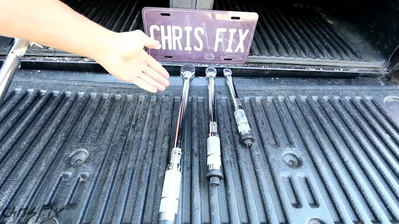 A hand gestures toward three torque wrenches of different sizes laid out on a truck bed, with a "CHRIS FIX" license plate in the background