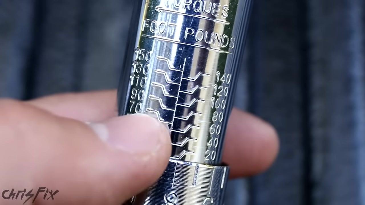 Close-up of a torque wrench scale with a finger pointing at the 100 foot-pounds mark