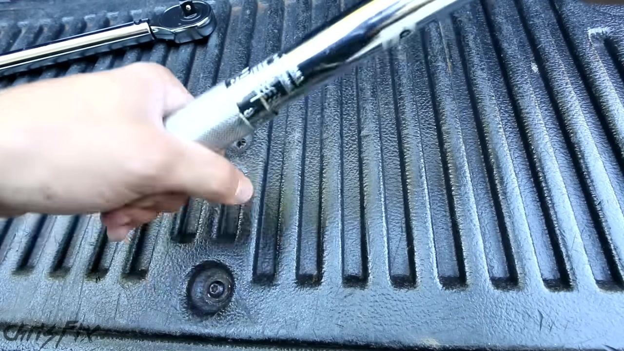 A person using a torque wrench with a socket to tighten a lug nut on a car wheel, showing proper hand placement and tool orientation
