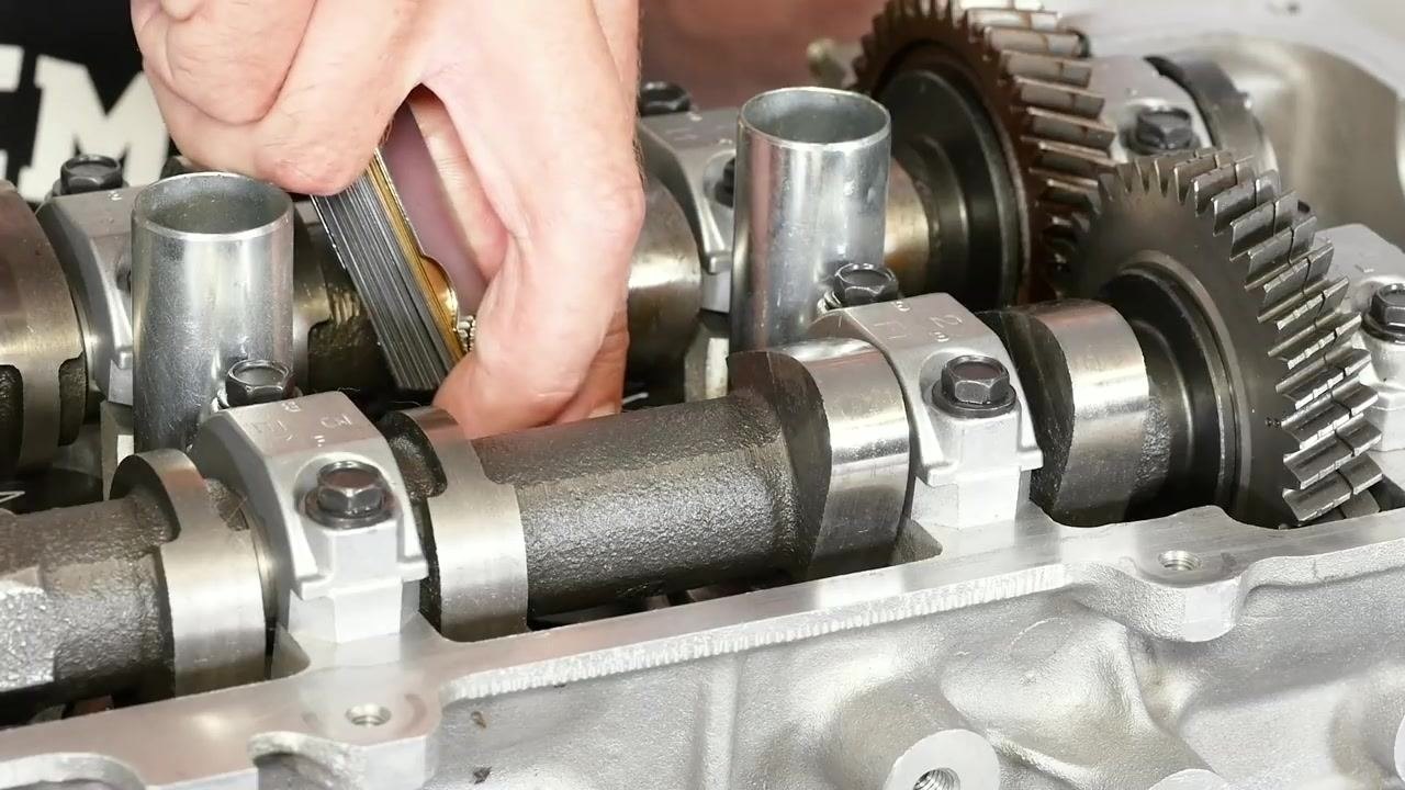 A close-up shows hands inserting a 0.010 inch (0.254 mm) feeler gauge between the camshaft lobe and the bucket on the cylinder head. The blade's thickness marking is visible.