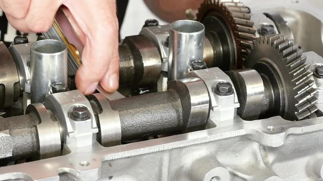 A close-up shows hands inserting a 0.013 inch feeler gauge between the camshaft and bucket, checking for resistance to confirm the correct clearance.
