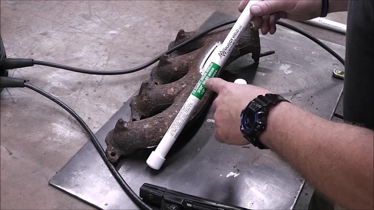 A person holds the welding rod above the cast iron part, demonstrating bead placement. The work area and tools are visible.
