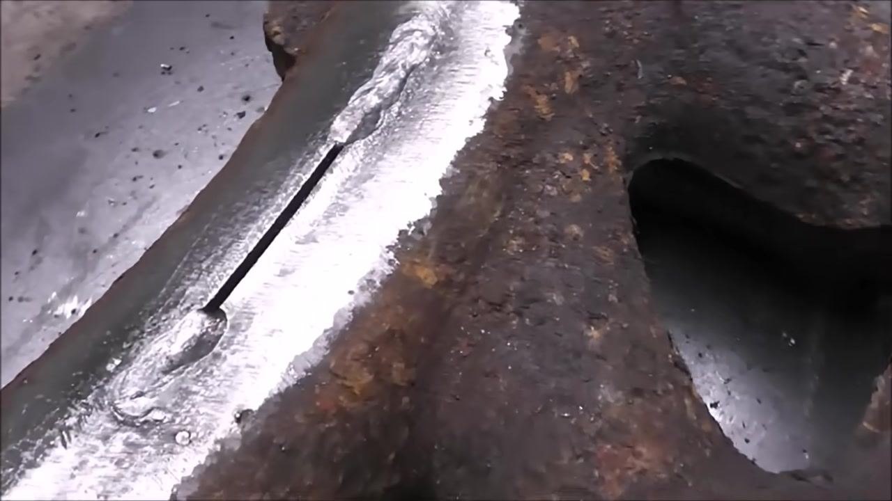 Close-up of a cast iron part with a shiny, freshly welded bead along a ground area. The rest of the part is rusty. No hands or tools are visible.