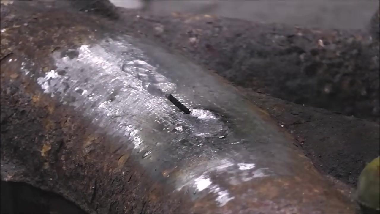 Close-up of a cast iron part with a shiny, ground weld area. The electrode is held at an angle, touching the weld, illustrating the "sharpening a pencil" motion.
