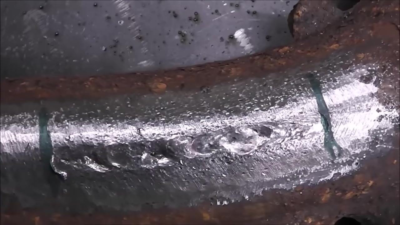 Close-up of the weld area with a shiny bead and scattered slag/spatter droplets on the cast iron part.