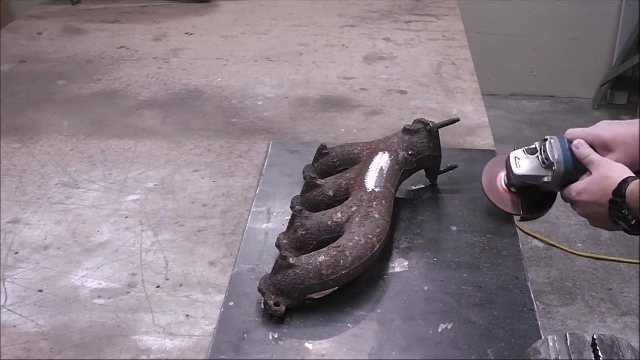 A close-up of the exhaust manifold with a shiny, ground area. A metal pointer indicates the start and end points of the visible crack.