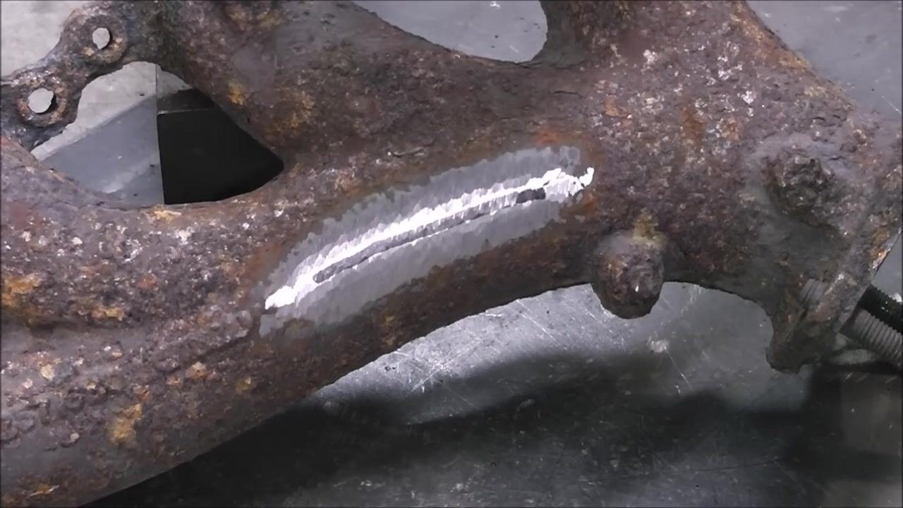 A close-up of the exhaust manifold with a shiny, ground area and a drilled hole at the end of the crack, as described in the preparation process.