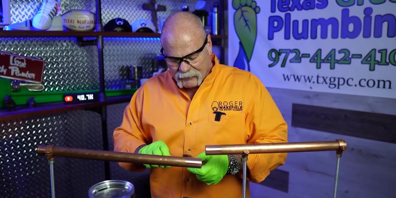A person inspects the placement of a green abrasive pad on a copper pipe before cleaning.