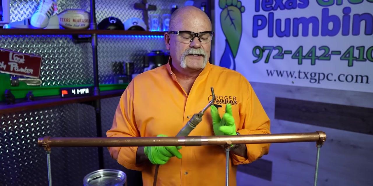 A person holds a soldering torch upright in a plumbing workshop, preparing for safe use.