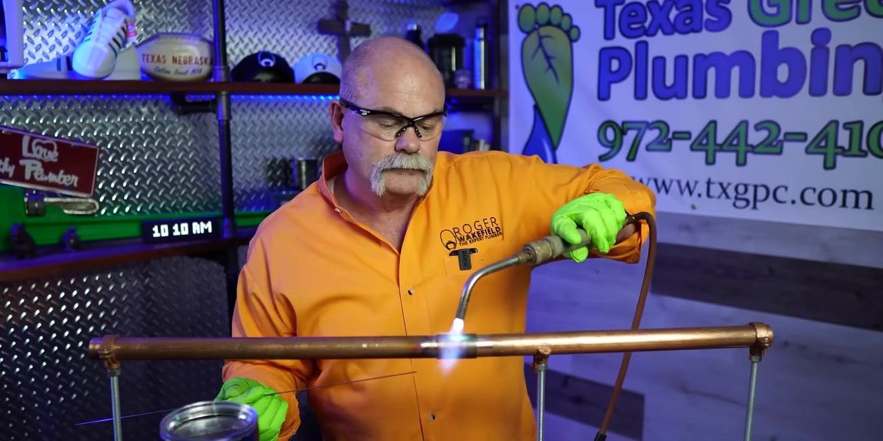 A person applies torch flame directly to a copper pipe joint, heating it for soldering.