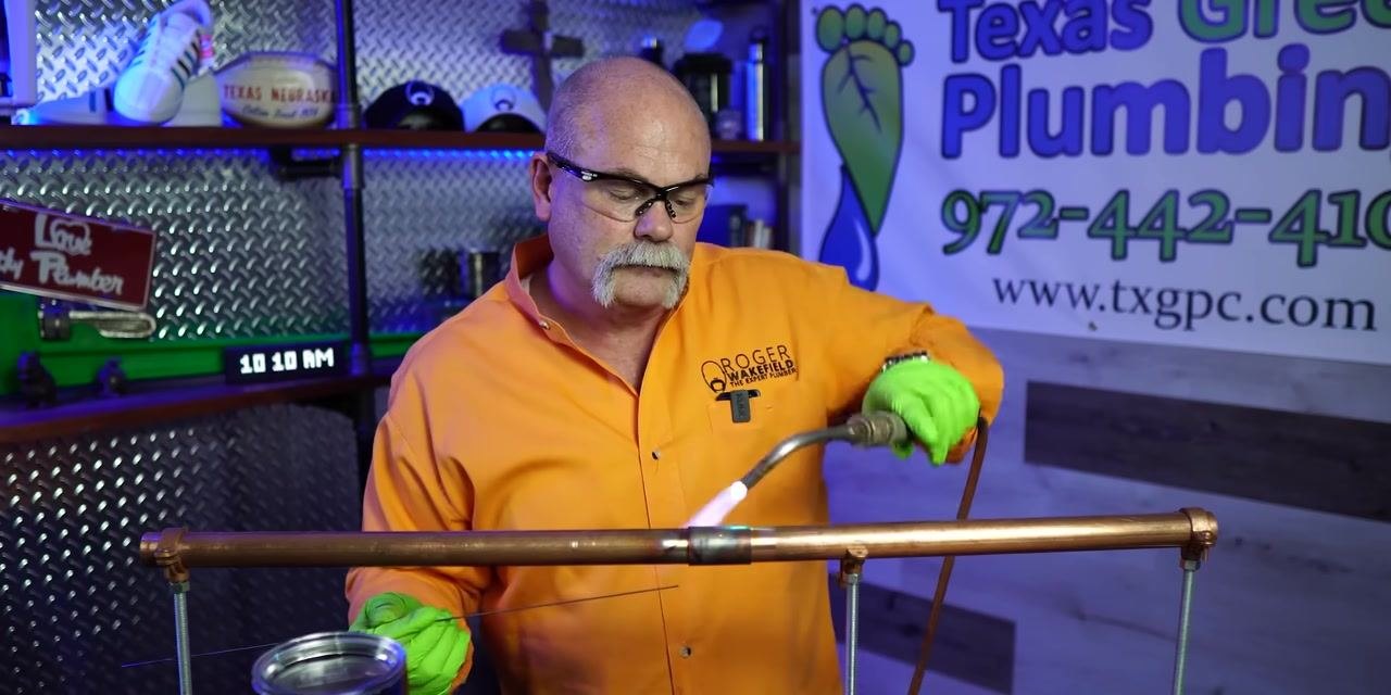 A person alternates between heating a copper pipe joint with a torch and applying solder wire.