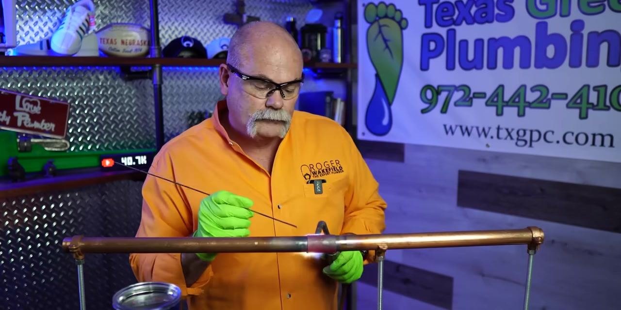 A person applies solder to a copper pipe joint while heating with a torch, ensuring a complete seal.