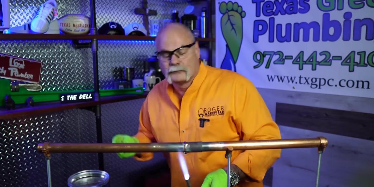 A person removes the torch from a completed soldered copper pipe joint, allowing it to cool.