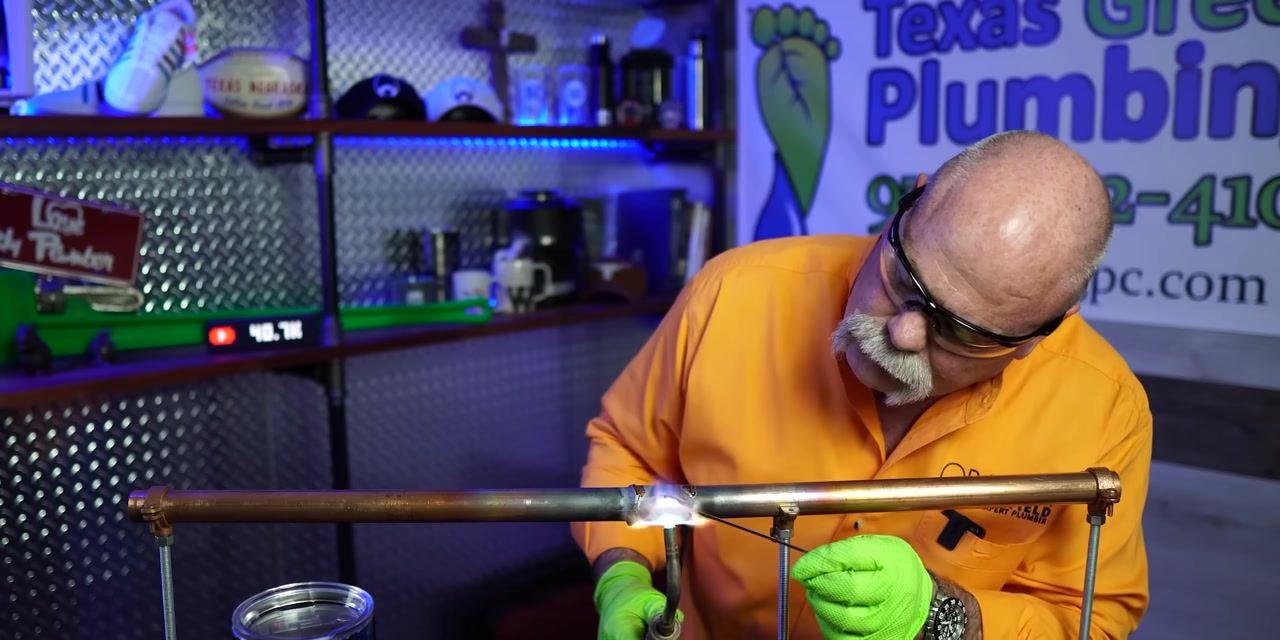 A person applies final heat and solder to a copper pipe joint, ensuring a complete and even seal.