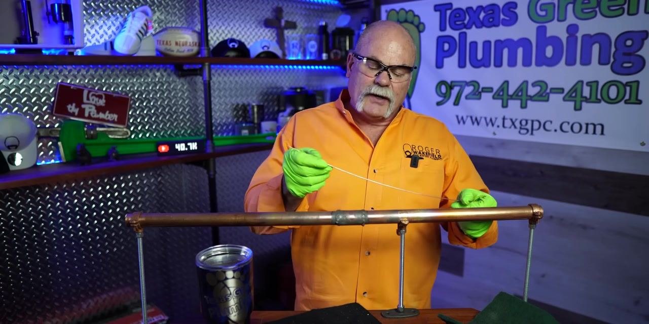 Instructor holding solder wire near the cleaned copper pipe joint, demonstrating proper solder application technique.