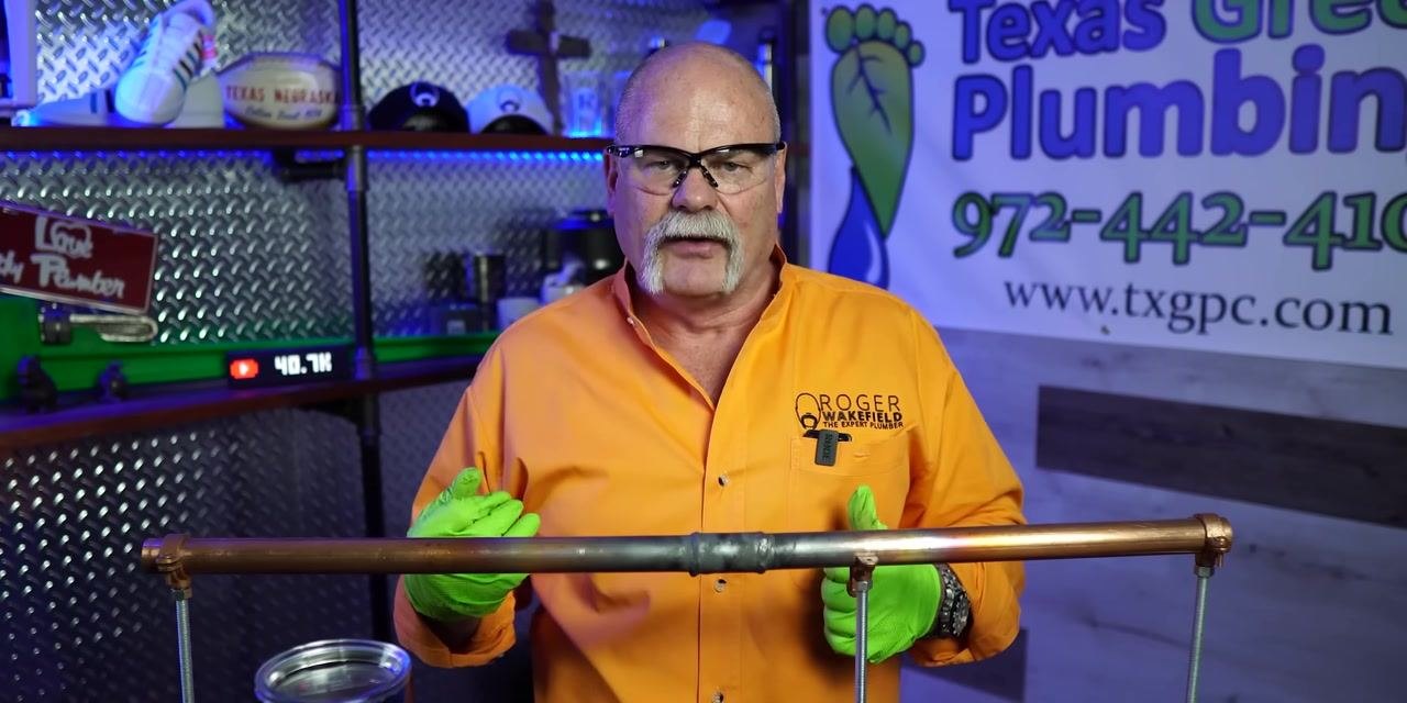 A person gestures toward a soldered copper pipe joint, emphasizing key inspection points.