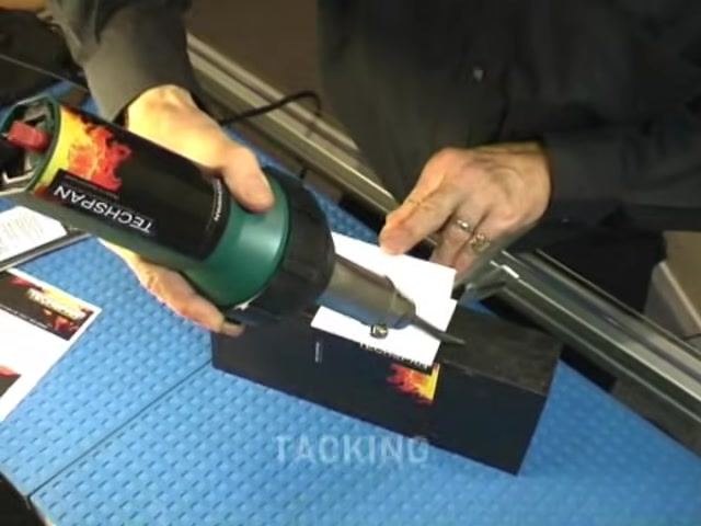 A person uses a TECHSPAN welding tool with a tacking nozzle to run along the joint of two plastic pieces, holding the materials in place on a blue work mat, with the word "TACKING" on screen