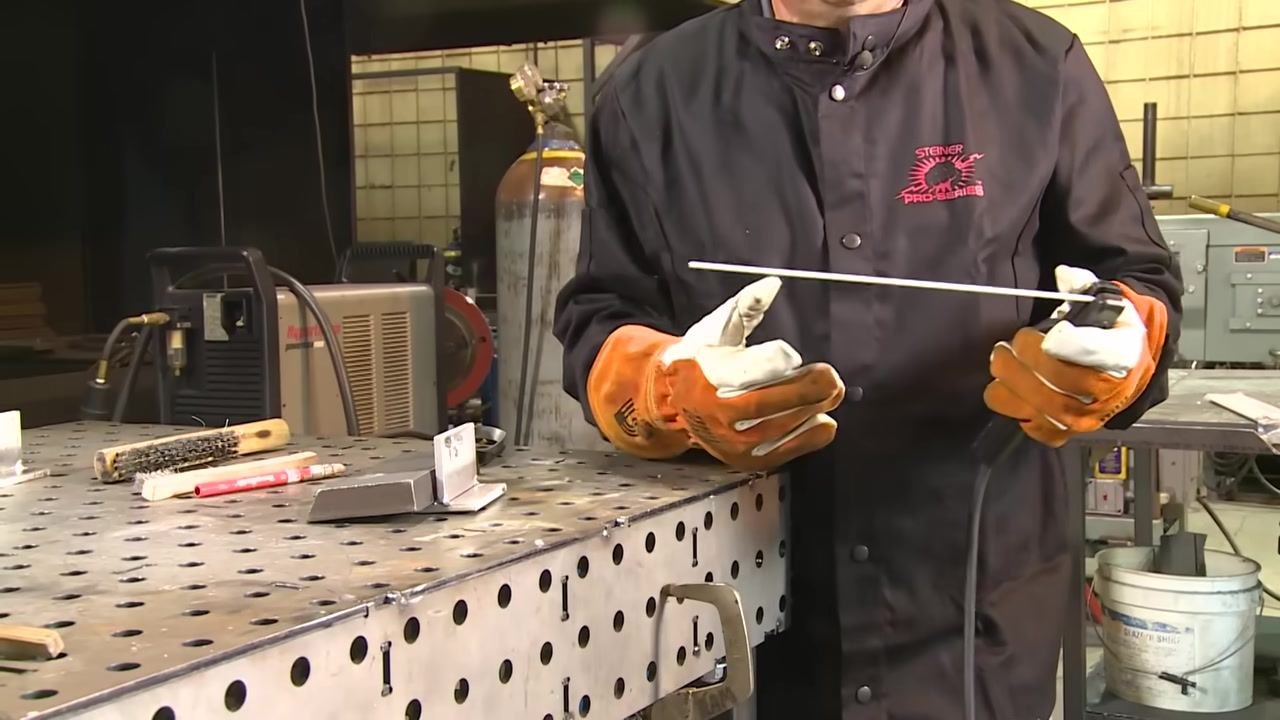 Close-up of the metal joint with tack welds visible on the perforated welding table.
