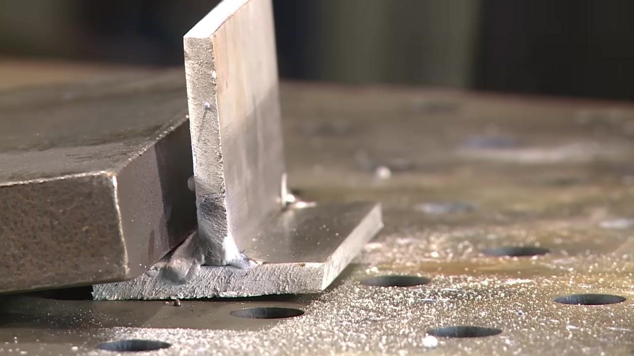 The welded joint on the perforated table, showing the results of the previous pass and some spatter, with no hands or tools in frame.