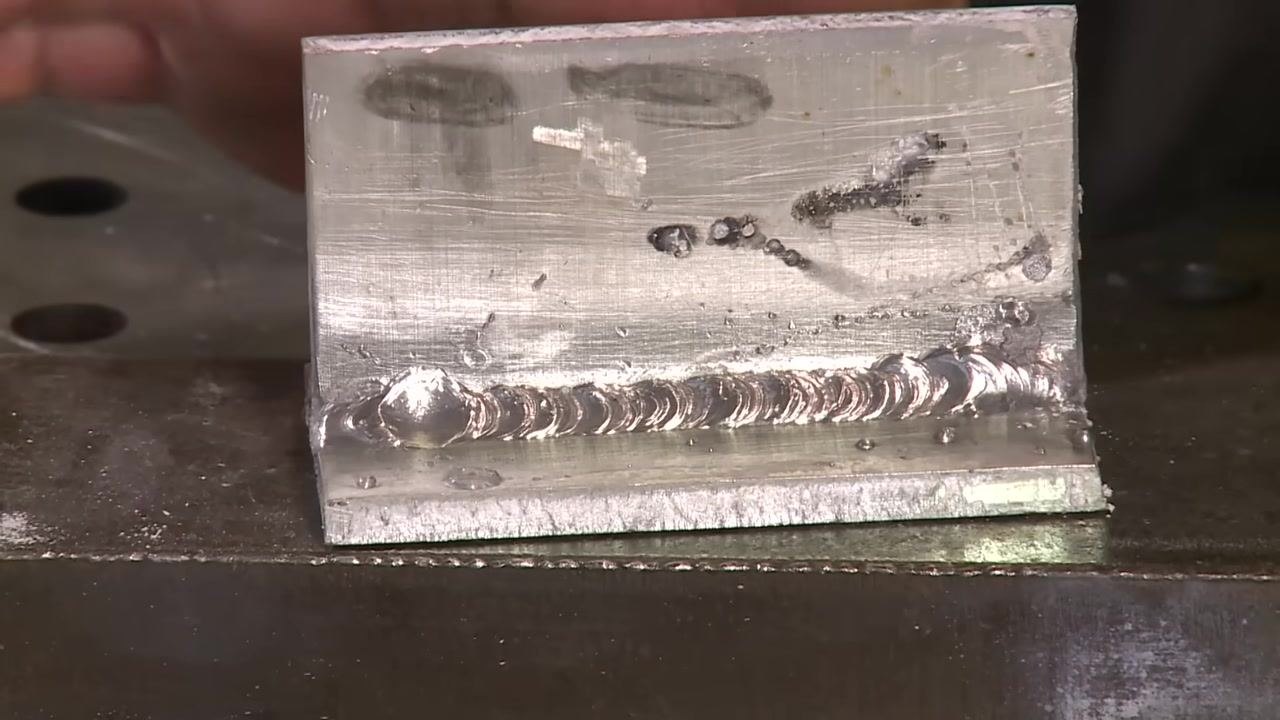 Aluminum weld with an excess blob and a hand holding a tool near the weld, ready for cleanup.