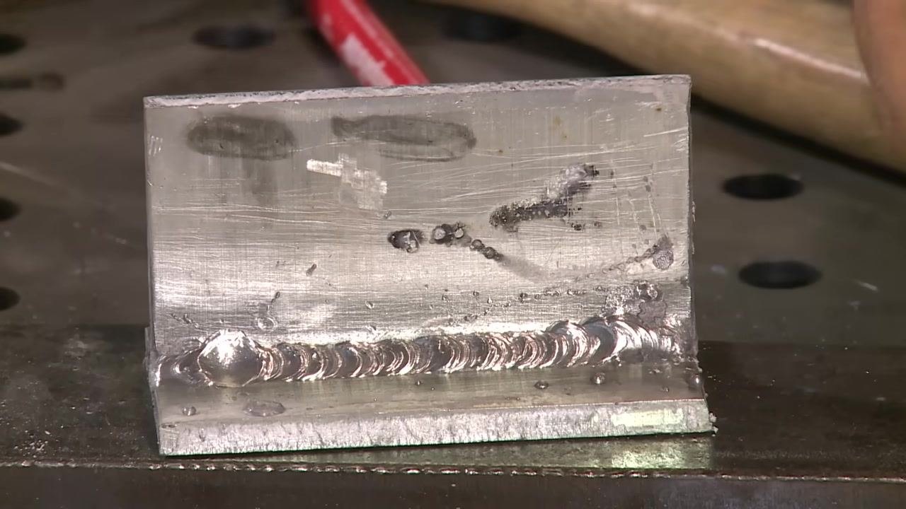 Aluminum weld with a visible bead profile and spatter, hand in background.
