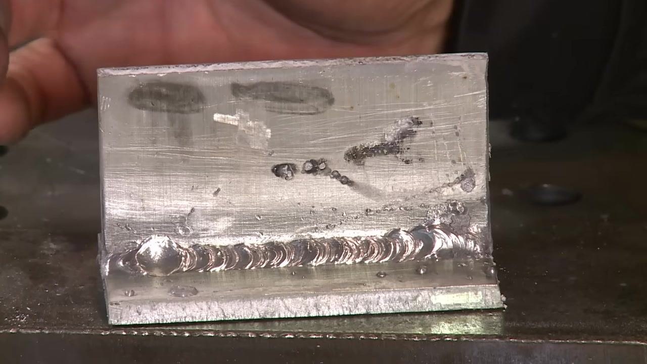 Aluminum weld with a hand gesturing near the weld to emphasize key points.