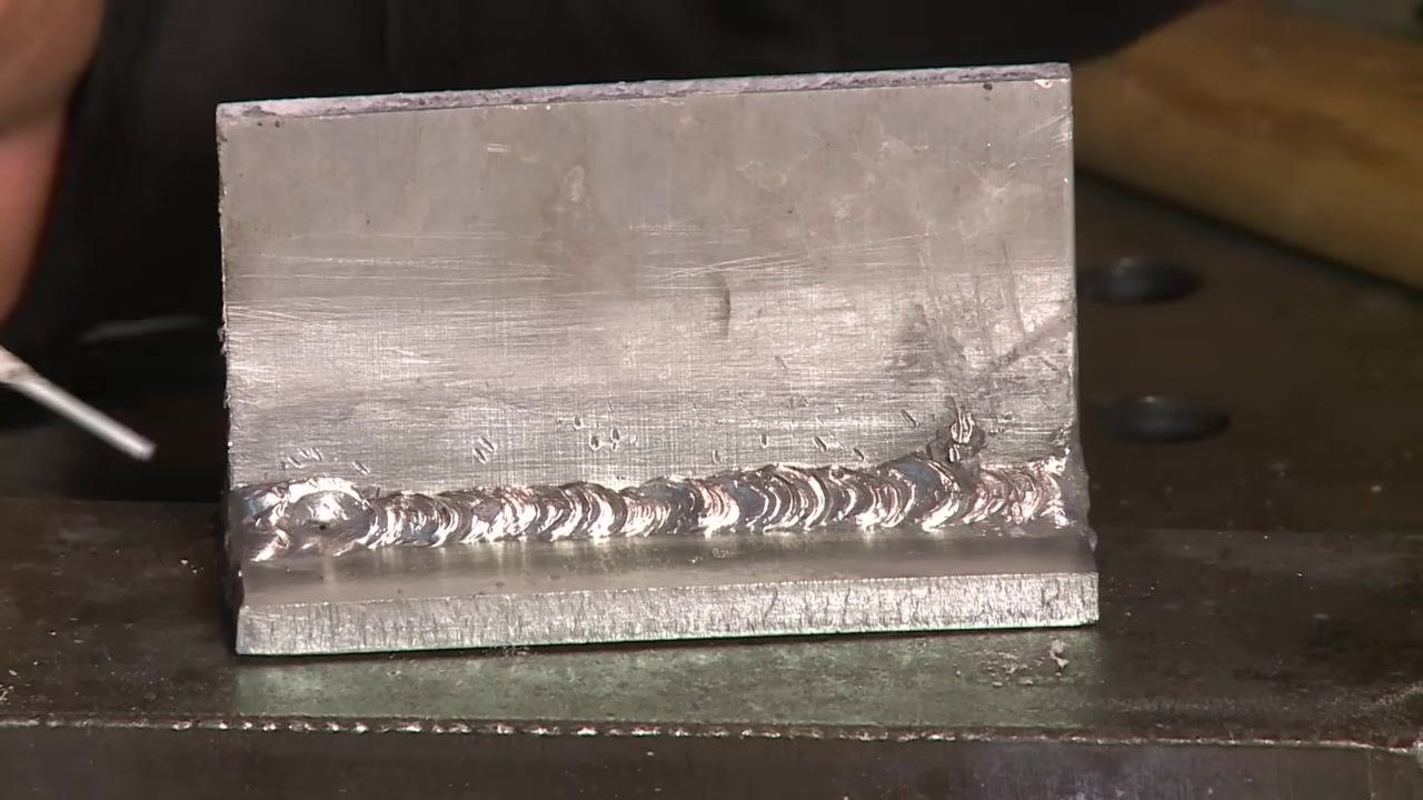 Aluminum weld bead with a hand and tool, illustrating finishing preferences.