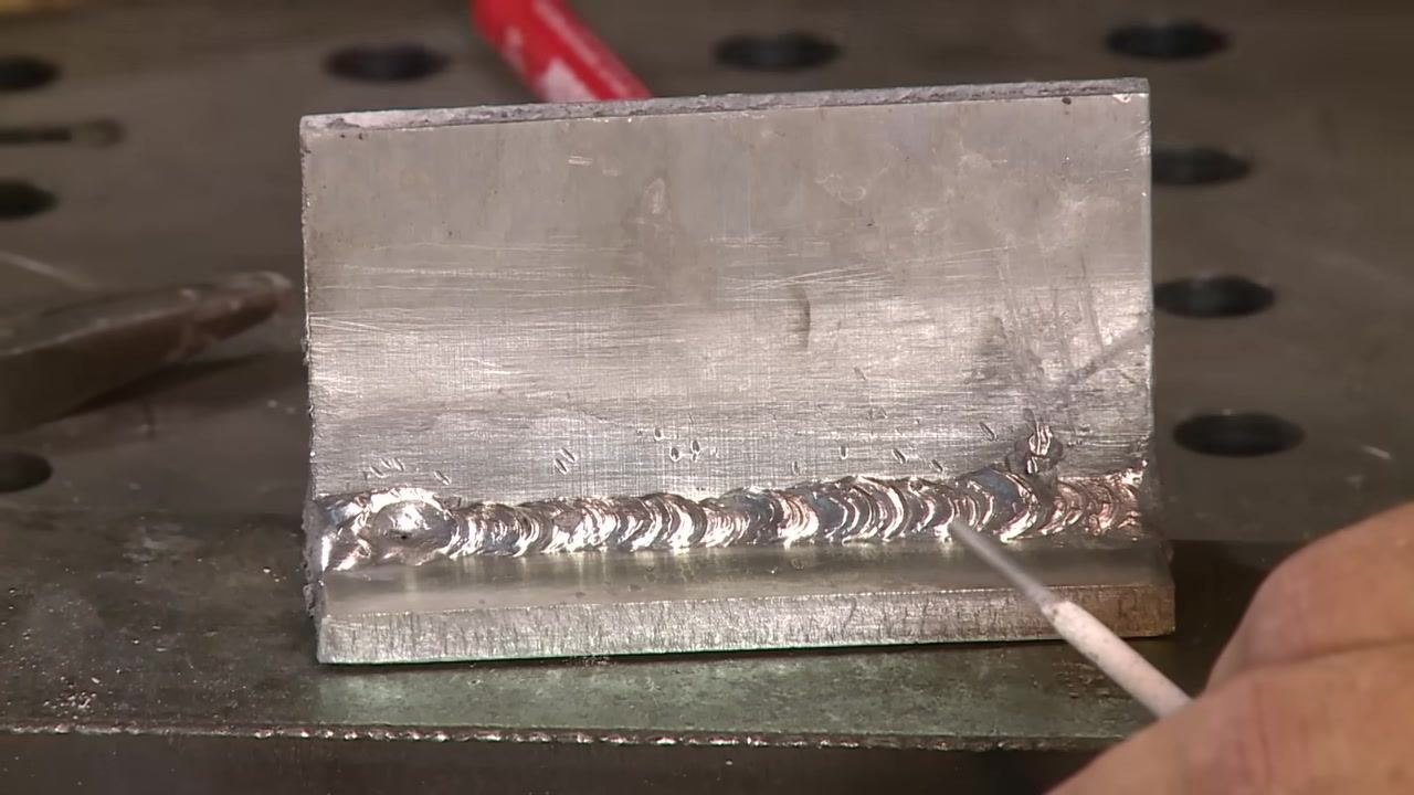 Aluminum weld with a hand pointing using a rod, highlighting features of the bead.