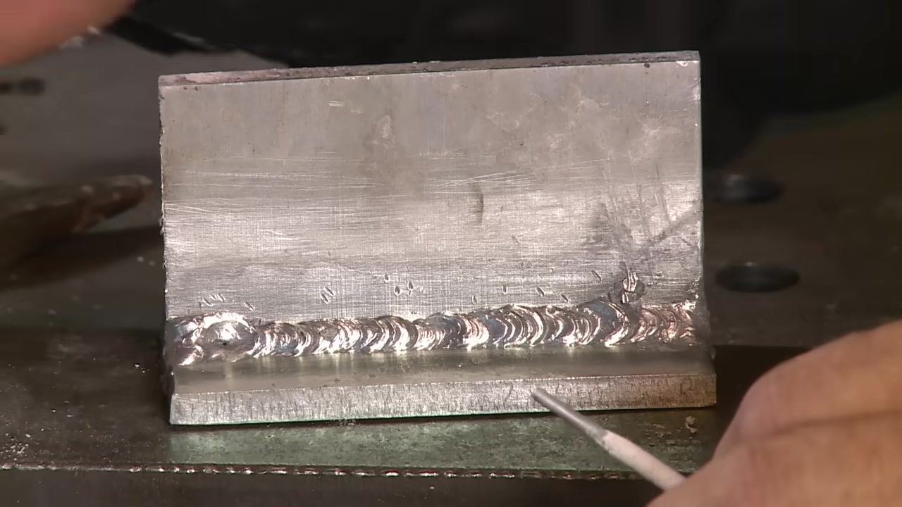 Close-up of the aluminum weld crater with a visible star hole, rod pointing at the defect.