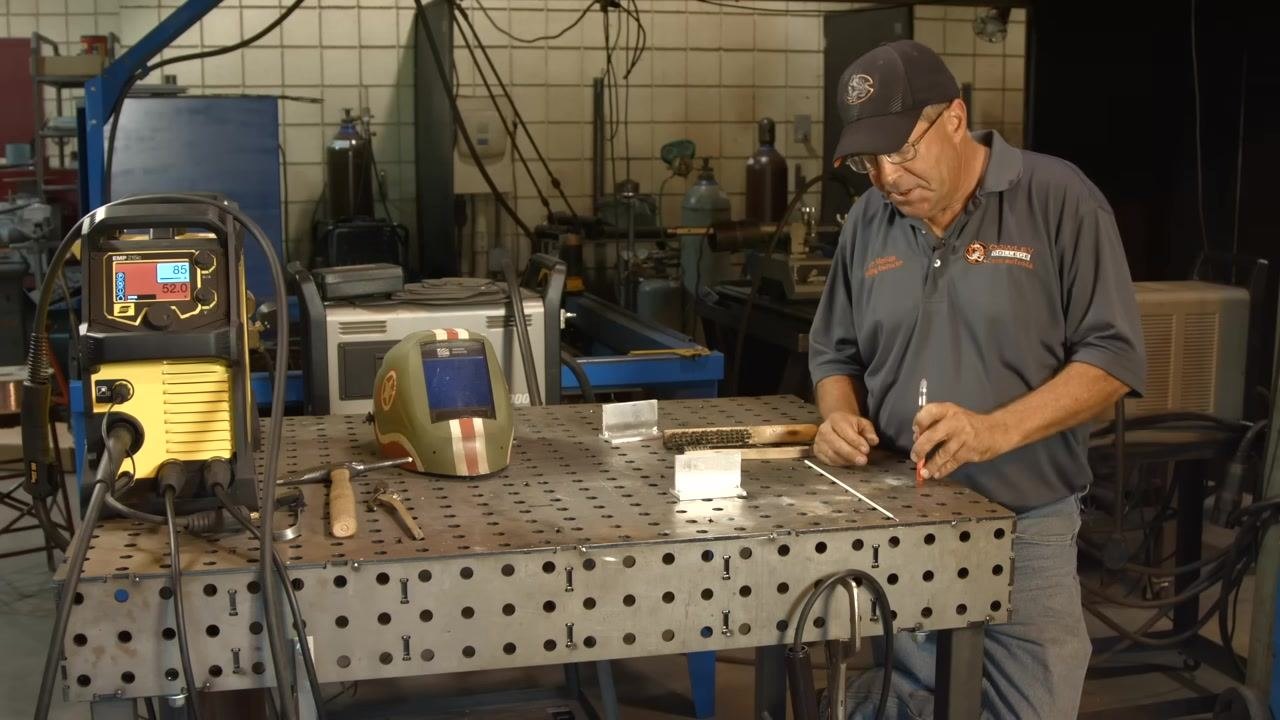Marking the aluminum workpiece with a Tempilstik in preparation for preheating, with the full workbench setup visible.