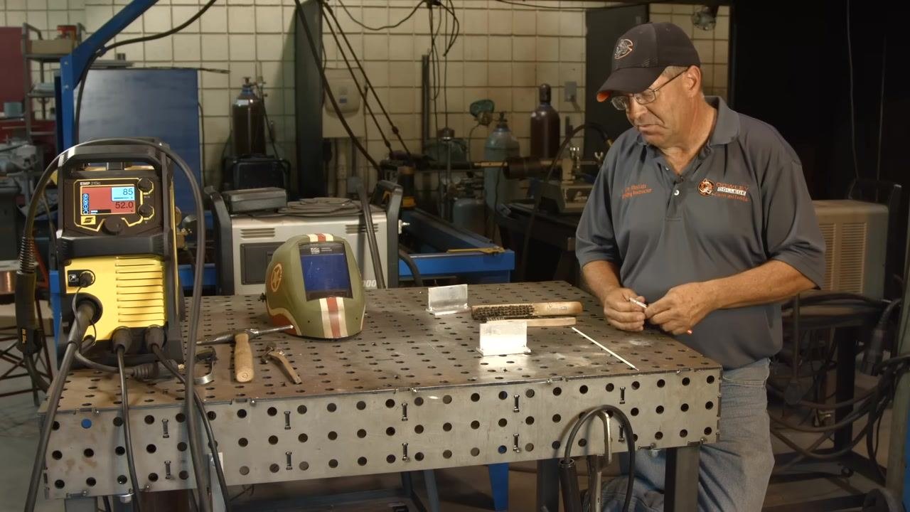 Wearing a welding jacket and gloves while holding an oxy-acetylene torch, preparing to apply soot to the aluminum workpiece.