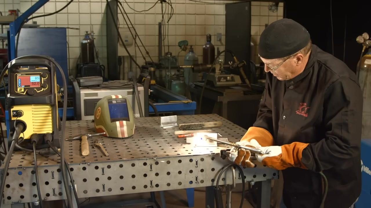 Using an oxy-acetylene torch to heat the aluminum workpiece, with a visible flame and protective gear in use.