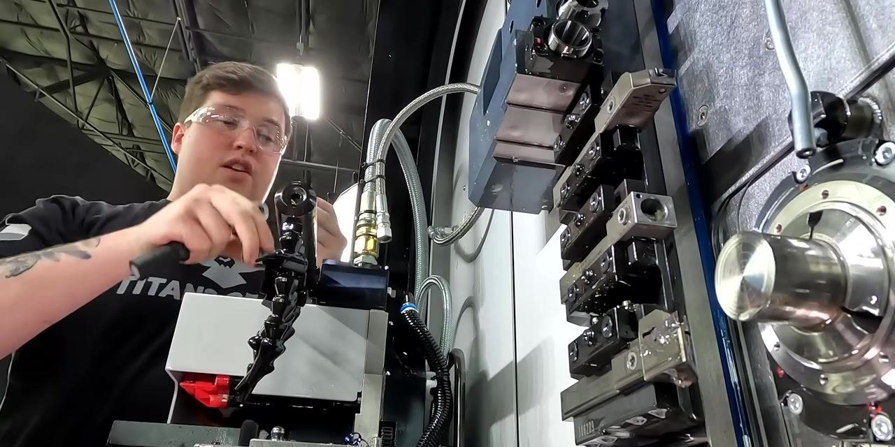 Person wearing safety glasses using a tool to remove an insert from a CNC tool holder, with multiple tool holders and machine components visible