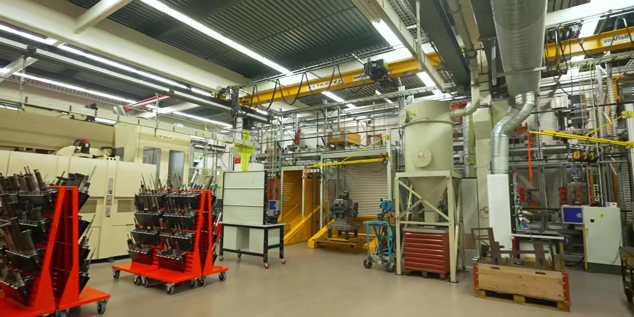 Wide view of a modern CNC shop floor with multiple machines, red tool racks, overhead cranes, dust collection units, and organized workstations.