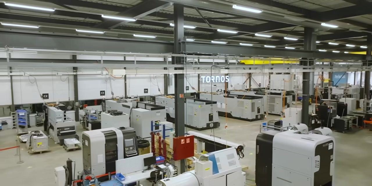 Wide view of a modern CNC machine shop with many machines and workstations, "TORNOS" sign visible.