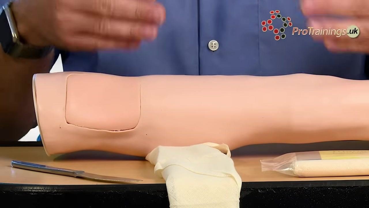A practice arm on a table with a triangular bandage and a knife positioned nearby, ready for tourniquet application.