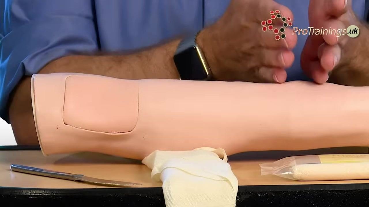 A practice arm with a triangular bandage tied around the upper arm, demonstrating tourniquet placement.