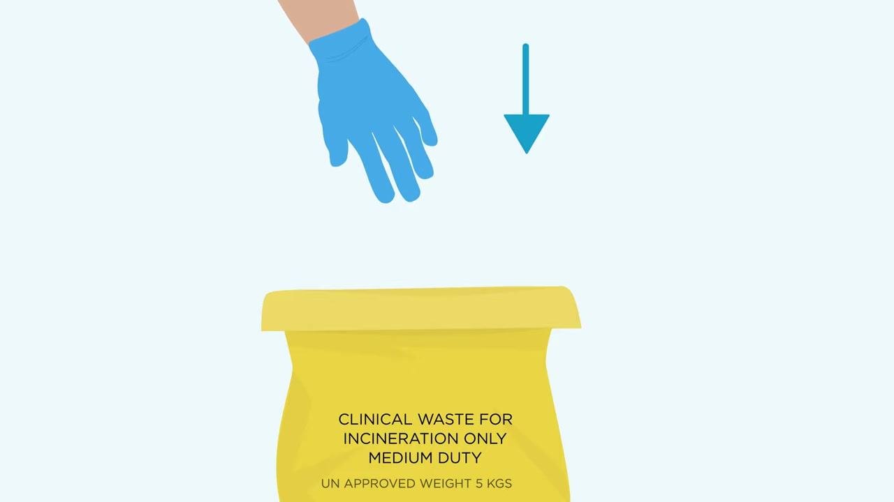 Gloved hand positioned above the yellow clinical waste bag, ready to dispose of the first removed glove