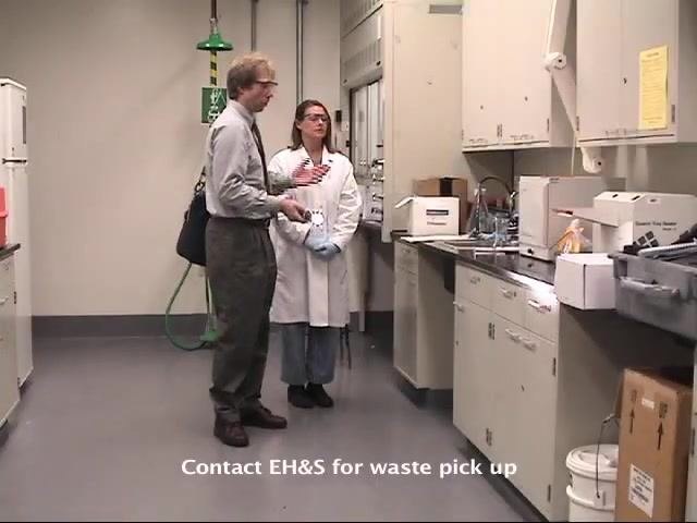 The EH&S staff member prepares to leave the laboratory as the worker stands nearby.