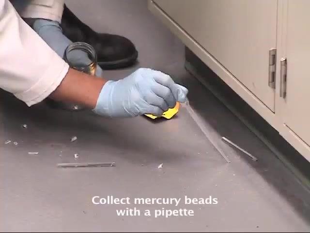 A gloved worker uses a pipette to collect mercury beads from the floor, with broken glass and the collection jar visible nearby.