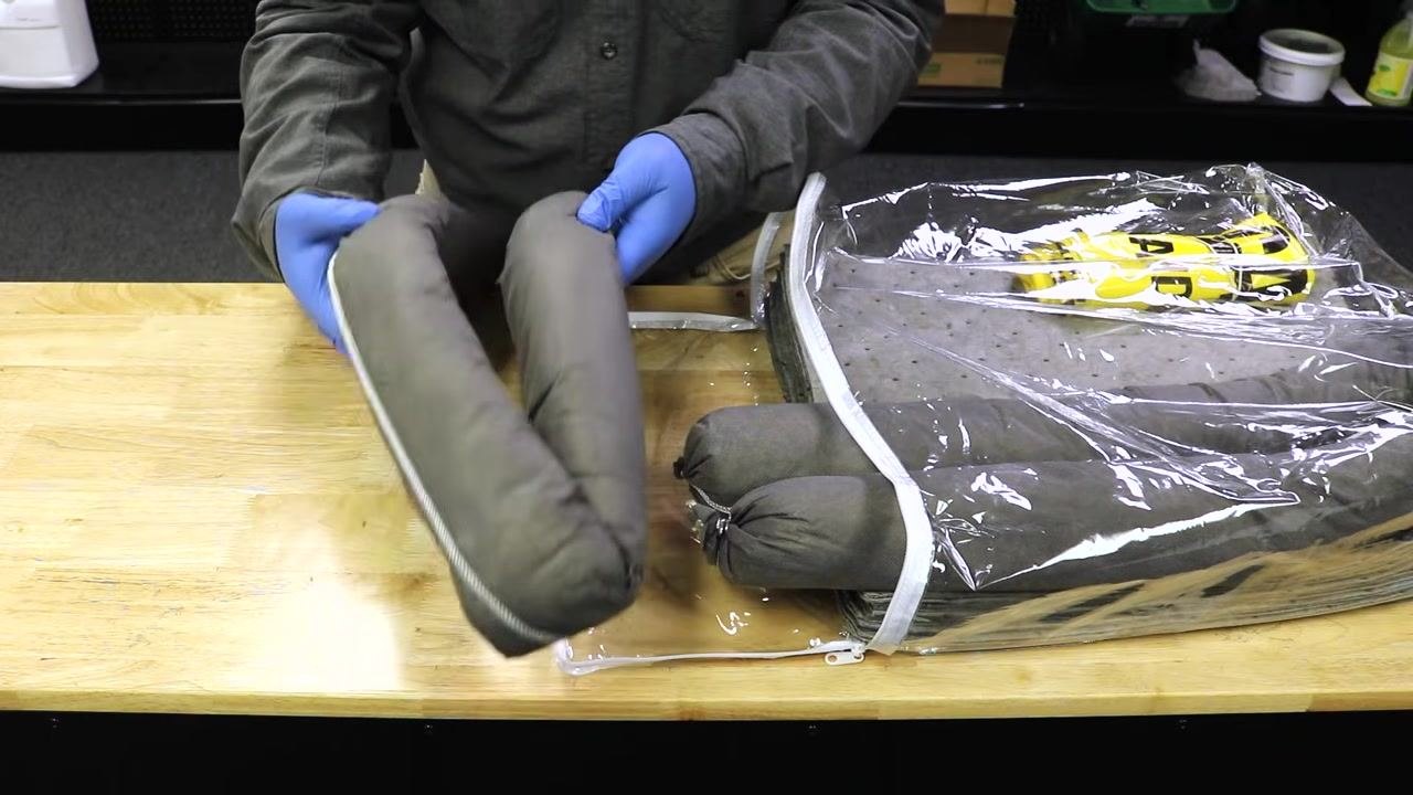 Person holding absorbent socks, preparing to place them back into the spill kit bag for storage or replacement